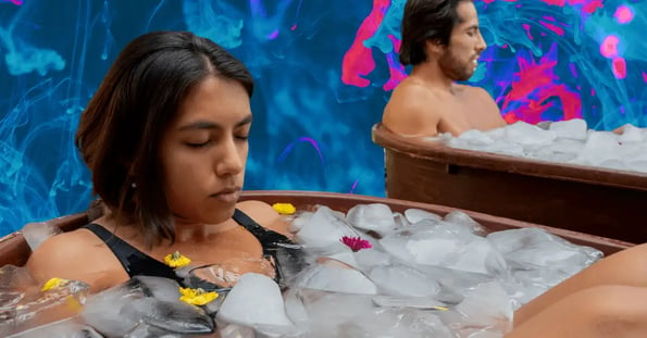 A man and a woman in copper tubs filled with ice cubes.